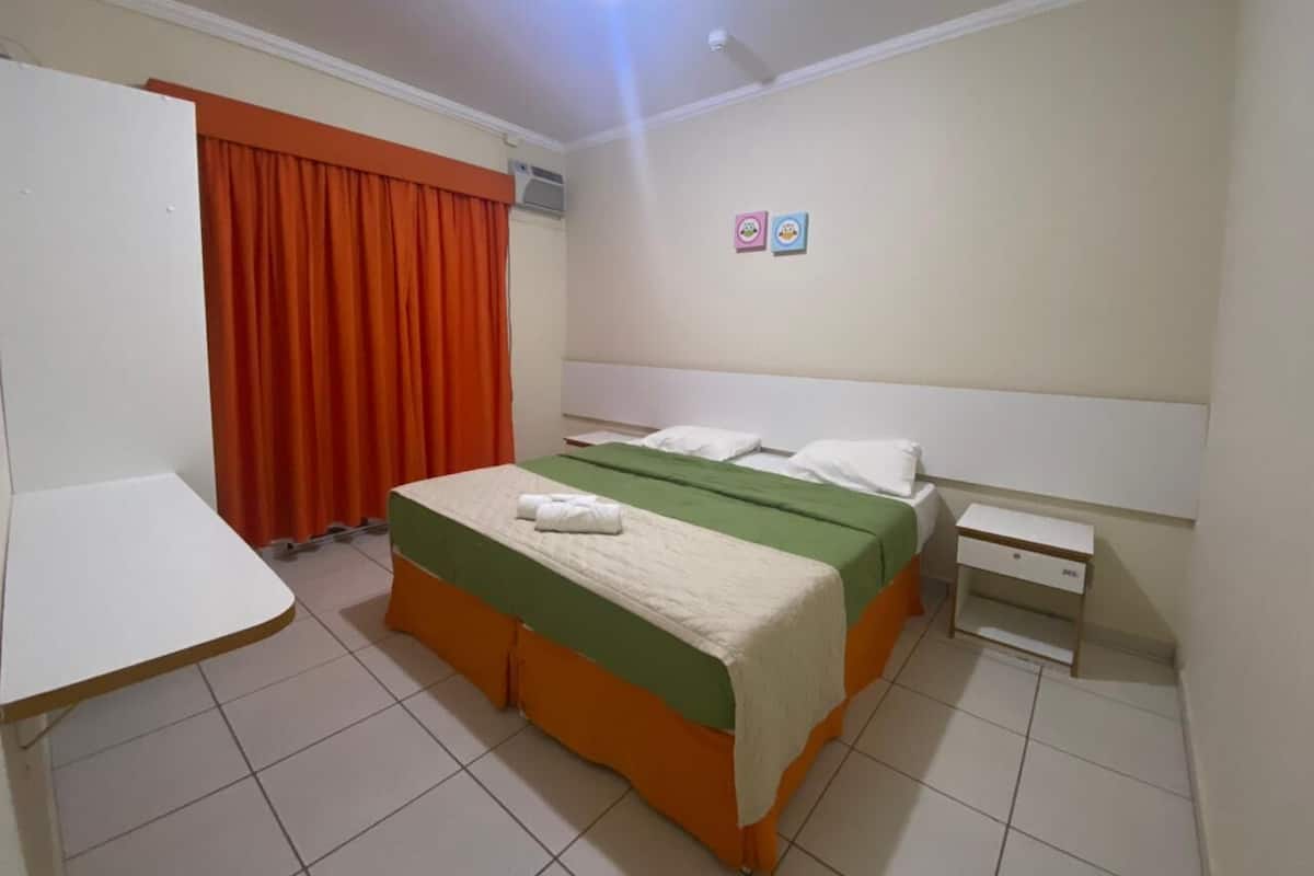 Una habitación de hotel con cama, mesita de noche, escritorio y ventana con cortinas.