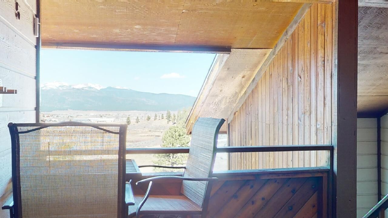 Een houten balkon met twee stoelen en uitzicht op een bergachtig landschap.