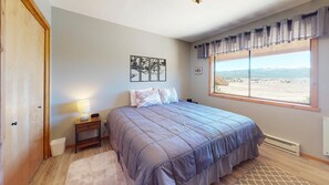 Um quarto com cama, mesa de cabeceira, luminária, janela com vista para o exterior e uma obra de arte na parede.