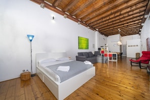 A bedroom with a wooden ceiling, a bed, a sofa, a dining table, and a red chair.
