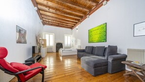 A spacious living room with a wooden ceiling, a grey sofa, a red chair, and a large abstract painting.