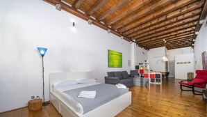 A bedroom with a wooden ceiling, a bed, a sofa, a dining table, and a red chair.