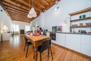 A spacious kitchen with wooden flooring, a wooden dining table, white cabinets, and a rustic ceiling.