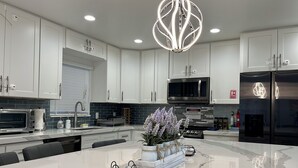 Una cucina moderna con mobili bianchi, un'isola centrale, un frigorifero in acciaio inossidabile e una lampada a sospensione originale.
