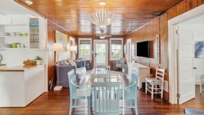 Una cocina amplia con paneles de madera, una isla central con pileta y una zona de comedor con mesa de vidrio y sillas azules.