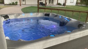 Een hottub met blauwe verlichting, omgeven door een houten terras en een gazon.