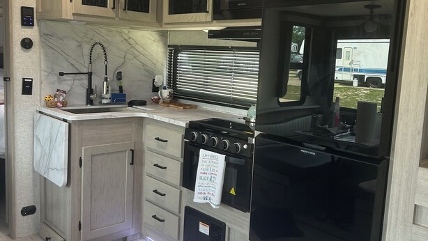 Een kleine RV-keuken met een kookplaat, oven en magnetron, houten kastjes en een raam met uitzicht.