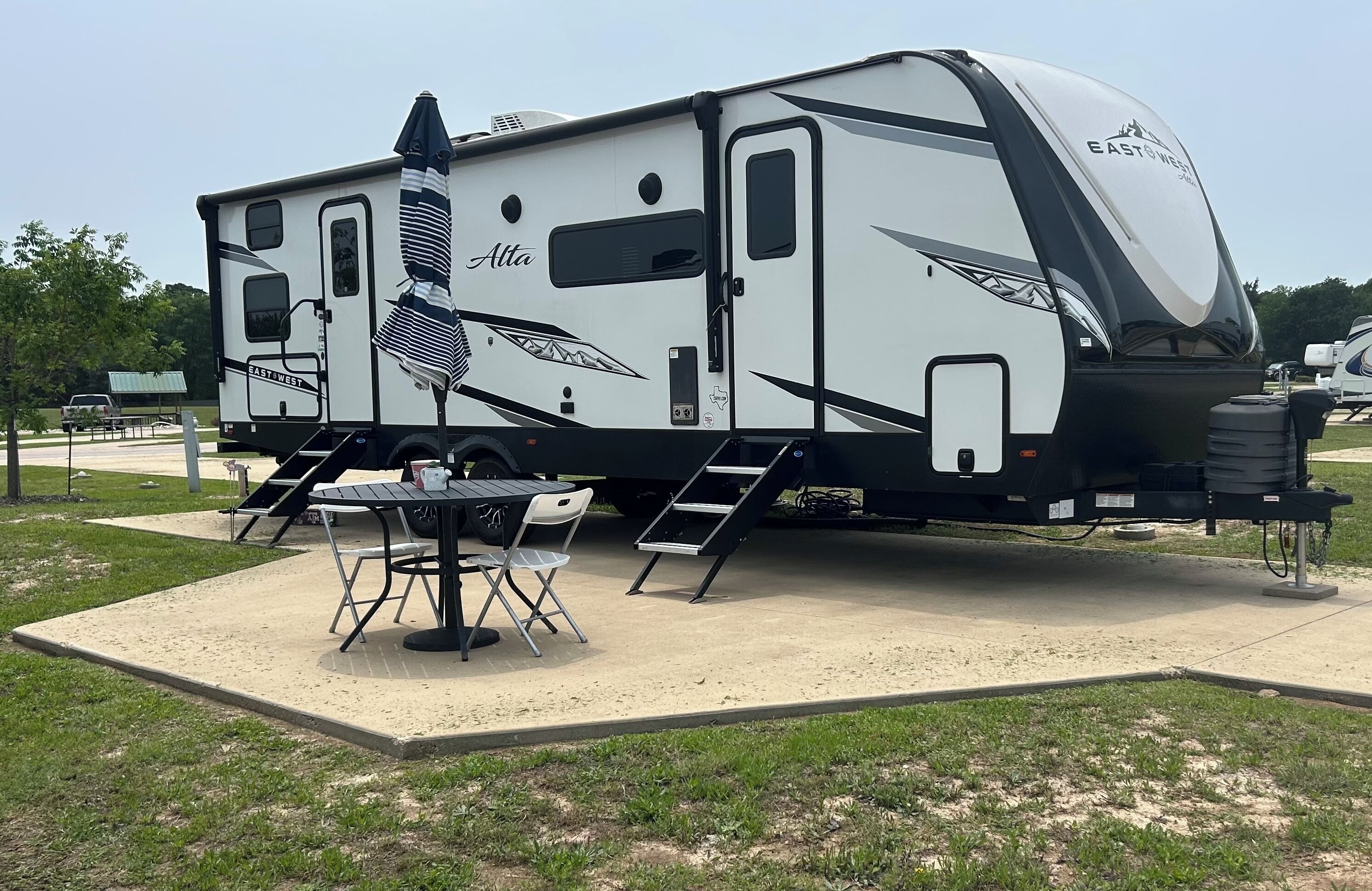 A recreational vehicle with a covered patio area, a table, and chairs.