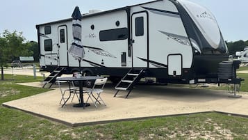 A recreational vehicle with a covered patio area, a table, and chairs.