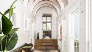 A hallway with white walls and wooden floors, leading to a living room with a sofa and a coffee table.