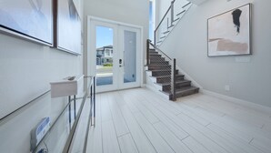 Un interior moderno con una escalera, una puerta que da al exterior y obras de arte en las paredes.