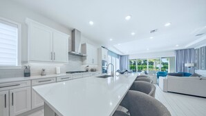 Una cocina moderna con armarios blancos, una isla grande y vistas a un área de estar al aire libre.