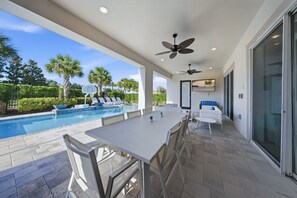 An outdoor pool area with a table and chairs, ceiling fans, and a view of the pool.