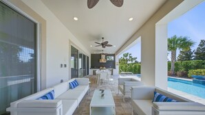 Un espacio exterior moderno con piscina, muebles blancos y ventilador de techo.