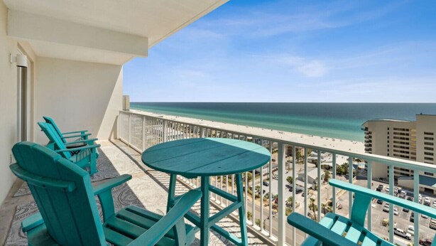 Un balcon avec des chaises turquoise et une table, donnant sur une plage et un parking.