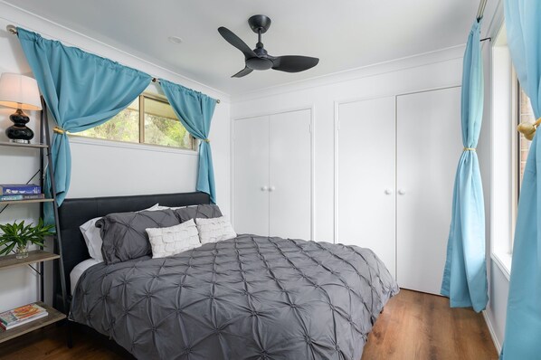 A bedroom with a bed, a ceiling fan, a wardrobe, and curtains.