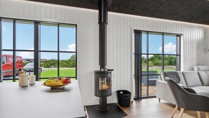 Een modern interieur met een houtkachel, grote ramen en uitzicht op de omgeving.