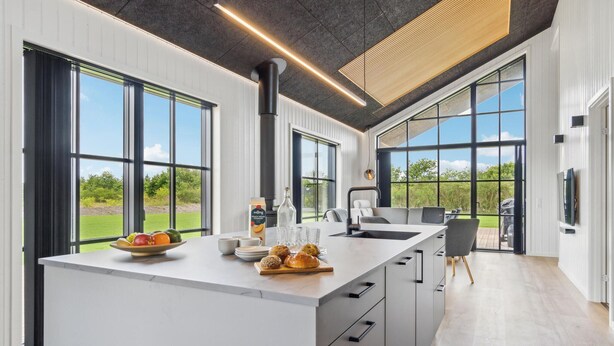 Een moderne keuken met grote ramen, een centraal eiland en uitzicht op de omgeving.