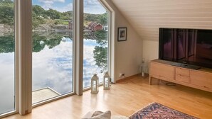 Quarto com grandes janelas que oferecem vista para um lago e casas, televisão de tela plana e um armário de madeira.