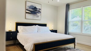 Une chambre à coucher moderne avec un lit, des tables de chevet, un tableau et une fenêtre avec des stores.