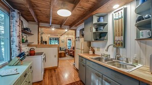 A cozy kitchen with wooden beams, a sink, and a dining area with a red kettle. - Quintessential Maine cabin w/ private waterfront (Augusta)