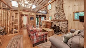 A rustic cabin interior with a stone fireplace, plaid sofas, and a wooden ceiling. - Quintessential Maine cabin w/ private waterfront (Augusta)