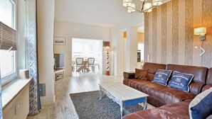 A living room with a sofa, a coffee table, and a TV. There is a dining area in the background. - Nilles Huuske - Luxusferienwohnung (Sellin)