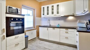 A kitchen with white cabinets, a microwave, an oven, a sink, and a window. - Nilles Huuske - Luxusferienwohnung (Sellin)