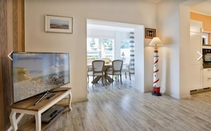 Ett vardagsrum med en tv, en matplats med stolar, en lampa och ett köksutrymme.