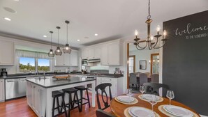 A modern kitchen with white cabinetry, a large island with bar stools, and a dining area with a wooden table set for four.