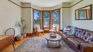A corner room with a bay window, a leather sofa, a coffee table, and a dining table with chairs.