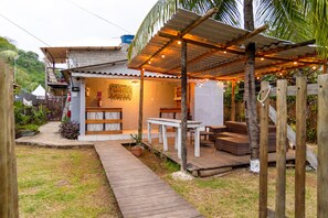 A wooden deck with a table and chairs, a covered seating area, and a small garden with a pathway. - Noronha Suites (Fernando de Noronha)