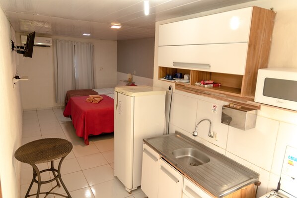 A compact hotel room with a kitchenette, a small dining table, a bed, and a TV. - Noronha Suites (Fernando de Noronha)