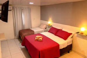 A hotel room with two beds, one with a red bedspread and the other with a brown bedspread. There are two bedside lamps, a TV mounted on the wall, and a window with curtains. - Noronha Suites (Fernando de Noronha)