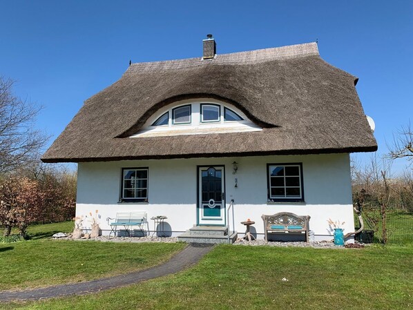 A traditional house with a thatched roof, a front door, and a small porch area with benches and a table.