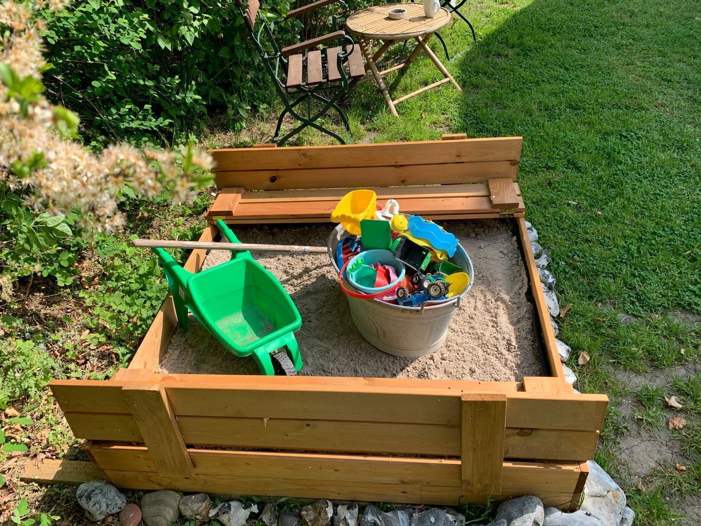 Ein hölzerner Sandkasten mit einer Schaufel und einem Eimer voller Spielzeug.