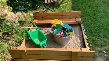Ein hölzerner Sandkasten mit einer Schaufel und einem Eimer voller Spielzeug.