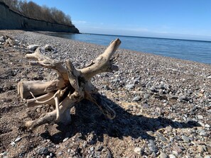 Un trozo de madera a la deriva sobre una playa pedregosa, con un mar tranquilo y acantilados al fondo.