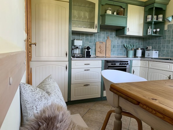 A kitchen with white cabinets, a wooden table, and a fluffy pillow on a bench.