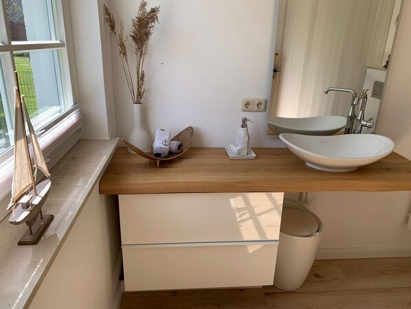 Un baño moderno con tocador de madera, lavabo blanco y espejo.