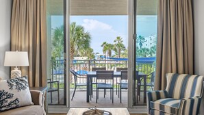 A room with a sofa, armchair, and a table with a decorative centerpiece. A sliding glass door leads to an outdoor patio with a table and chairs.