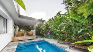 Ein modernes Haus mit Swimmingpool, umgeben von üppiger tropischer Vegetation.