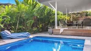 Una piscina con un porche cubierto, rodeada de exuberante follaje tropical.