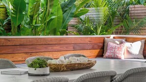 Un banco de madera con cojines y una mesa de mimbre con una planta y un cuenco de piedras.