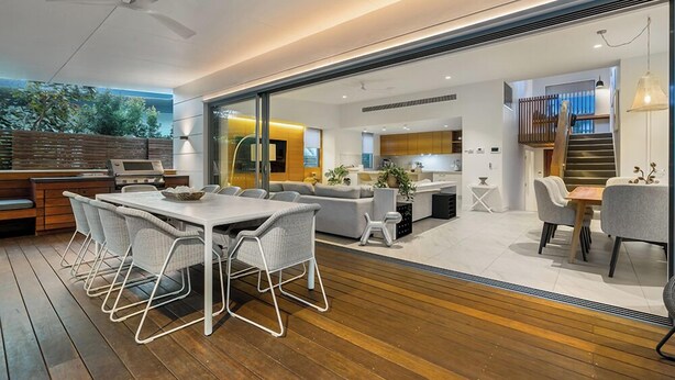Una cocina moderna con horno empotrado, un comedor con mesa y sillas de madera, y una escalera que conduce a un nivel superior.