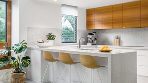 Una cocina moderna con una isla central, taburetes de bar, armarios de madera y una cafetera.