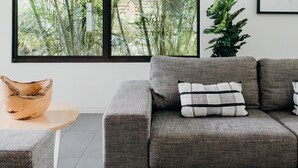 Un salon moderne avec un canapé gris, une petite table en bois et une grande fenêtre donnant sur un paysage verdoyant.