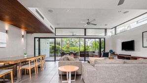 Un salon moderne avec un grand canapé, une table à manger avec des chaises, une table basse ronde et un téléviseur fixé au mur.