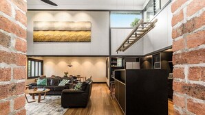Een modern interieur met een bakstenen muur, een zwarte zithoek, een houten salontafel, en een keuken met een zwarte koelkast.