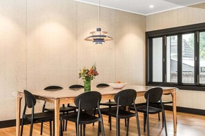 A dining area with a wooden table, black chairs, a vase with flowers, and a pendant light.